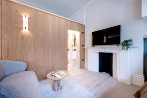 Ein modernes Wohnzimmer mit Sofa, rundem Couchtisch, flachbildfernseher über einem Kamin und einer Holzwand mit integrierter Beleuchtung.