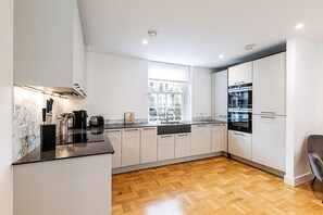 A modern kitchen with white cabinetry, a marble backsplash, and a wooden herringbone floor. - Modern and Elegant Apartment in West Kensington (London)