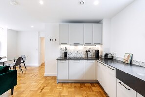 Eine moderne Küche mit weißen Schränken, einer Marmor-Spritzschutzwand und einem Essbereich mit einem grünen Stuhl.