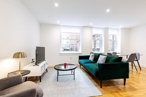 Ein modernes Wohnzimmer mit einem grünen Sofa, einem Fernseher, einem Couchtisch und einem Essbereich mit Stühlen.