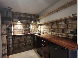 A kitchen with exposed brick walls, wooden countertops, a sink, and a dishwasher. - Architect Designed Studio Borough (London)