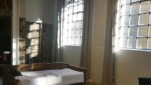 A room with a bed, a window with a grid pattern, and a stone wall. - Architect Designed Studio Borough (London)