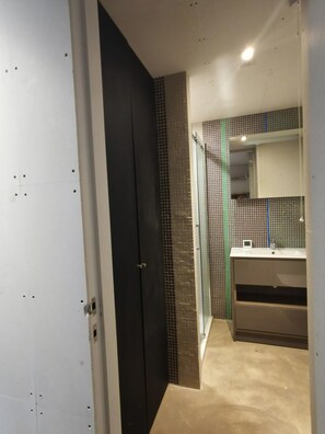 A modern bathroom with a dark door, tiled walls, a glass shower enclosure, and a sink with a mirror. - Architect Designed Studio Borough (London)