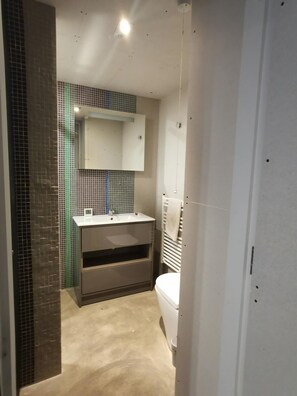 A bathroom with a tiled wall, a white sink, a mirror, and a toilet. - Architect Designed Studio Borough (London)