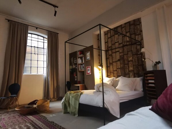 A bedroom with a four-poster bed, a bookshelf, a window with curtains, and a patterned rug. - Architect Designed Studio Borough (London)