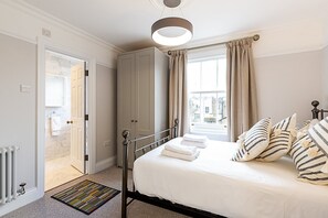A bedroom with a bed, a radiator, a door leading to a bathroom, and a window with curtains. - Stylish Marylebone City Apartment (London)