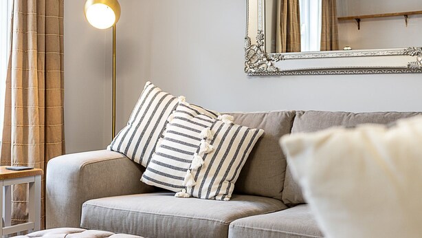 A living room with a sofa, striped pillows, a floor lamp, and a mirror. - Stylish Marylebone City Apartment (London)