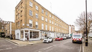 A multi-story building with a corner entrance, a row of shops on the ground floor, and a parked car in front. - Stylish Marylebone City Apartment (London)