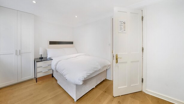 A bedroom with a bed, bedside table, and wardrobe. - Refined Pimlico Townhouse (London)