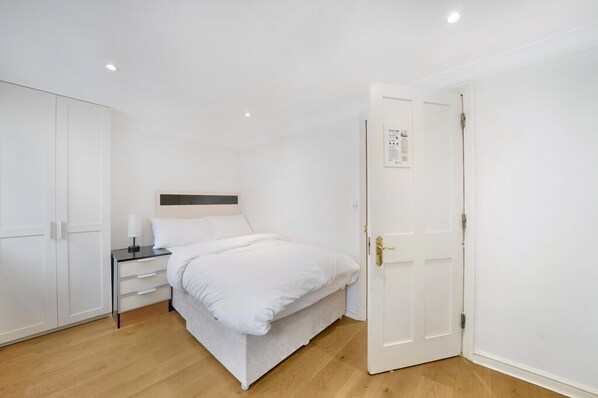 A bedroom with a bed, bedside table, and wardrobe. - Refined Pimlico Townhouse (London)