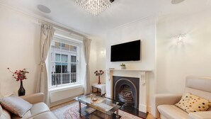 A living room with a fireplace, a sofa, a coffee table, and a TV mounted on the wall. - Refined Pimlico Townhouse (London)