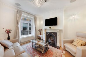A living room with a fireplace, a sofa, a coffee table, and a TV mounted on the wall. - Refined Pimlico Townhouse (London)