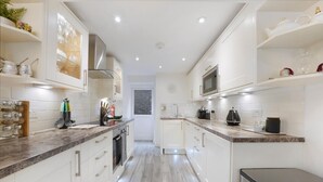 A modern kitchen with white cabinetry, a microwave, and a stainless steel trash bin. - Refined Pimlico Townhouse (London)