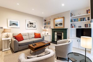Ein modernes Wohnzimmer mit Sofa, Sessel, Couchtisch, Kamin, Bücherregal und Fernseher.