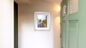 A hallway with a framed picture of a street scene, a green door, and a light fixture. - Chelsea Retreat With Private Patio (London)