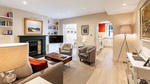 A modern living room with a fireplace, bookshelves, a sofa, and a dining area. - Chelsea Retreat With Private Patio (London)