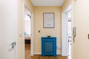 A hallway with a framed map of London, a blue side table with a bowl, and a phone on the wall. - Bow Retreat Near Victoria Park (London)