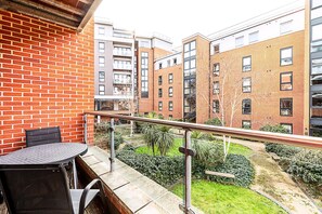 A balcony with a table and chairs, a brick wall, and a view of a courtyard with buildings and greenery. - Bow Retreat Near Victoria Park (London)