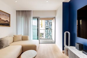 A modern living room with a sofa, a coffee table, a TV, and a large window with a view of buildings. - Stylish 2-bed by The O2 With Balcony (London)
