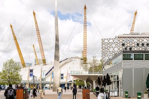 A modern building with a unique facade, a prominent central column, and a series of cranes. - Stylish 2-bed by The O2 With Balcony (London)