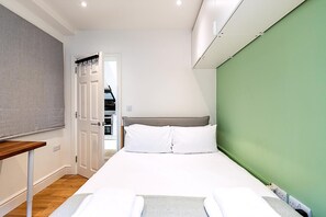 Ein Schlafzimmer mit einem Bett, einem Nachttisch aus Holz, einer grünen Wand und einer weißen Tür.