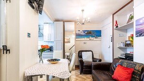A compact living space with a dining table, a leather sofa, a painting, and a kitchenette. - London Home With Garden Near Richmond Park (London)