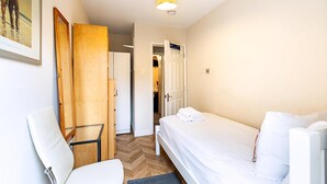 A bedroom with a bed, a chair, a wooden wardrobe, and a door leading to another room. - London Home With Garden Near Richmond Park (London)