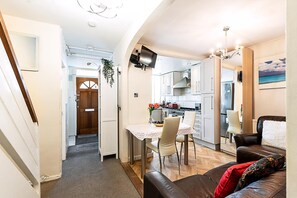 Eine kompakte Küche mit modernen Geräten, ein Essbereich mit Tisch und Stühlen sowie ein Wohnbereich mit Ledersofa.