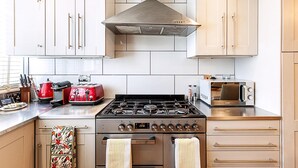 A kitchen with a gas stove, oven, microwave, and a range hood. There are cabinets and a countertop with various appliances and utensils. - London Home With Garden Near Richmond Park (London)