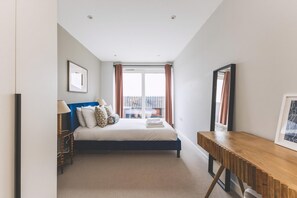 A bedroom with a bed, bedside table, lamp, and a view of the outside. - Stylish Wimbledon Flat With Balcony (London)