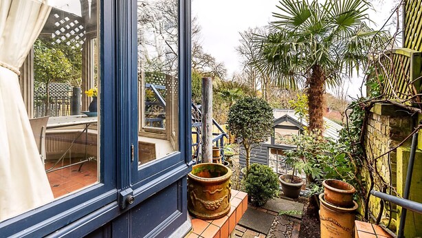 A window with a view of a garden, including potted plants and a palm tree. - Elegant Highgate Garden Retreat (London)
