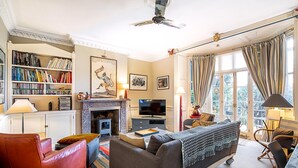 A living room with a fireplace, bookshelves, a television, and a sofa. - Elegant Highgate Garden Retreat (London)