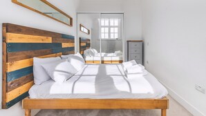 Une chambre à coucher avec une tête de lit en bois, un lit avec une literie blanche, un miroir et un placard à portes coulissantes.