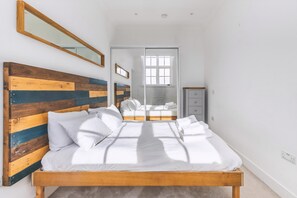Ein Schlafzimmer mit hölzernem Kopfteil, einem Bett mit weißer Bettwäsche, einem Spiegel und einem Schiebetürenschrank.