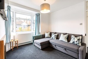 Ein modernes Wohnzimmer mit einer Eckcouch, einem kleinen Tisch und einem großen Fenster mit Vorhängen.