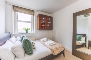 Une chambre à coucher avec un lit, des oreillers, une fenêtre, une armoire et un miroir.