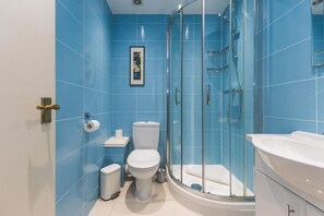 Une salle de bain avec des carreaux bleus, des toilettes, une poubelle, un espace douche et une baignoire.