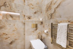 A bathroom with marble walls, a white toilet, a gold towel rack, and a gold flush handle. - Elegant South Kensington Retreat (London)