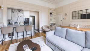 A modern living room with a sofa, a dining table, a kitchen area, and a bar with stools. - Elegant South Kensington Retreat (London)
