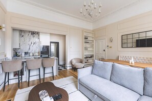 A modern living room with a sofa, a dining table, a kitchen area, and a bar with stools. - Elegant South Kensington Retreat (London)