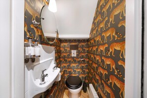 A bathroom with a leopard print wall, a white sink, a toilet, and a mirror. - Charming Pimlico Townhouse (London)