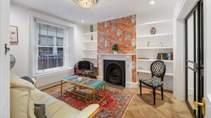 Ein Wohnzimmer mit Kamin, Bücherregal, einem zebra-gemusterten Sessel und einem farbenfrohen Teppich.