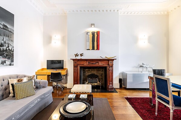 A living room with a fireplace, a sofa, a dining table, and a TV. - Boutique Kensington Retreat Near Museums (London)