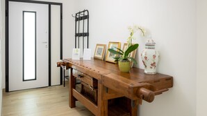 Una mesa de madera con un florero y fotografías enmarcadas, una puerta con marco negro y un perchero en la pared.