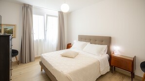 Un dormitorio con cama, mesitas de noche, cómoda y ventana con cortinas.