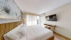 Quarto moderno com cama grande, televisão de tela plana na parede e escrivaninha de madeira.