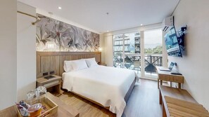 Habitación de hotel moderna con una cama grande, un escritorio, un balcón con vistas y un mural en la pared.
