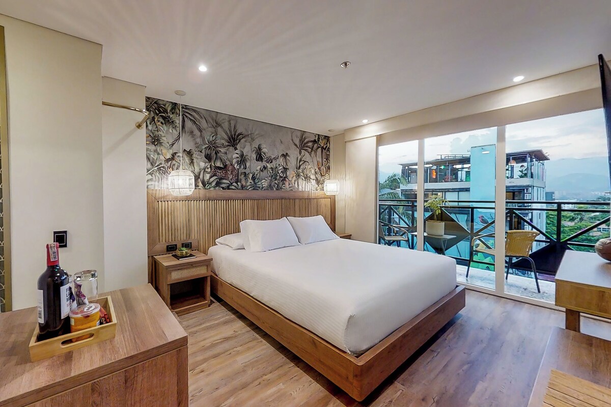 A modern hotel room with a large bed, wooden headboard, and a balcony with a city view.