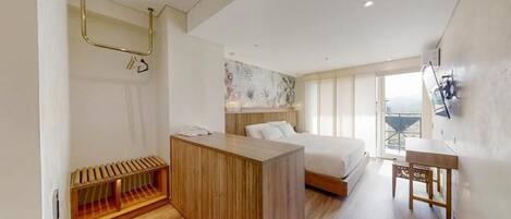 A modern hotel room with a wooden desk, a bed with white bedding, a large window, and a wall-mounted TV.