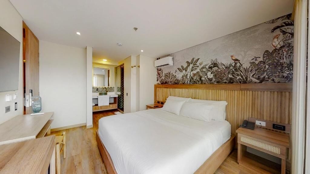 Habitación de hotel con una cama grande, una mesita de noche de madera, un escritorio y un aire acondicionado de pared.